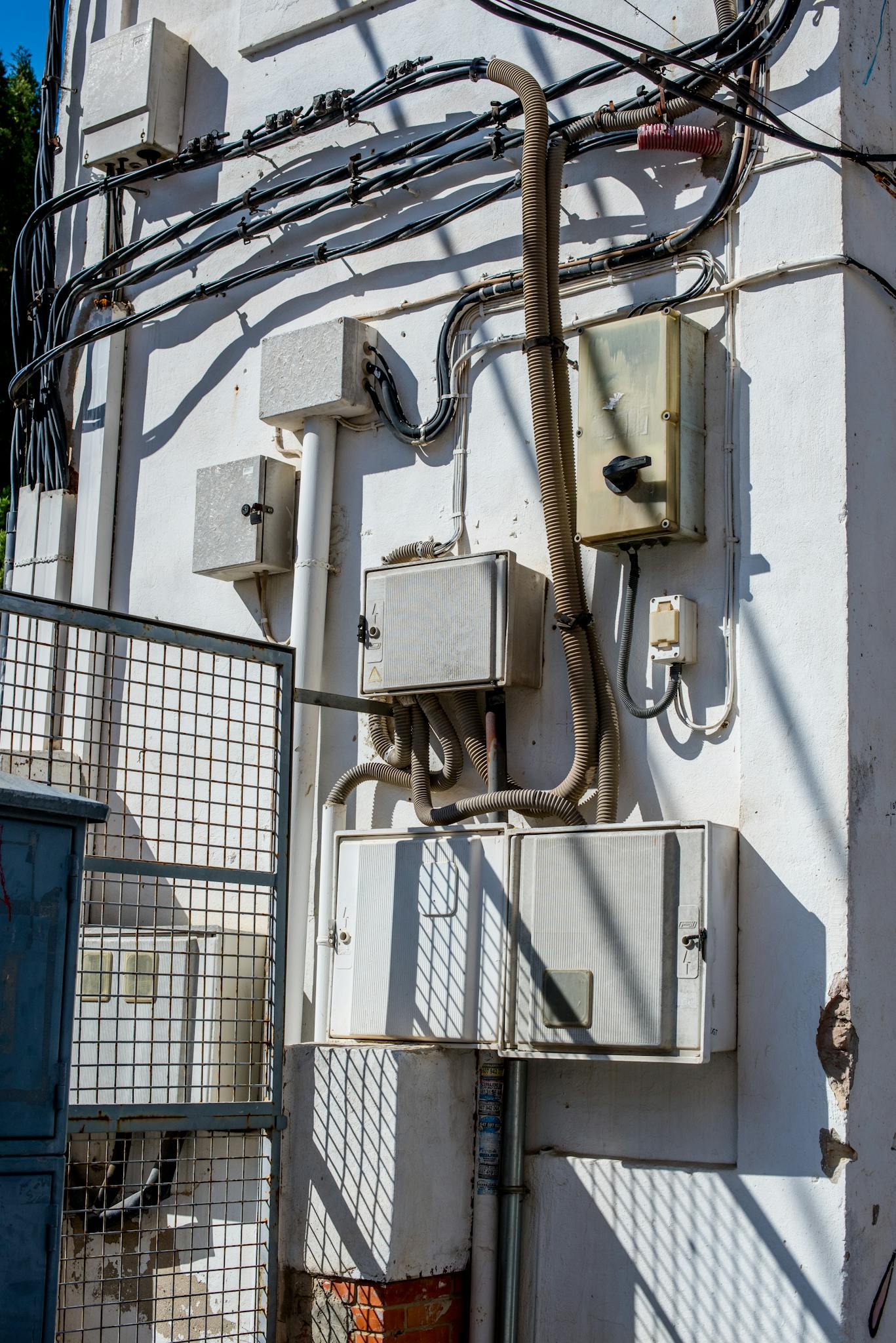 Close-up of outdoor electrical boxes and wiring system mounted on a white wall in daylight.